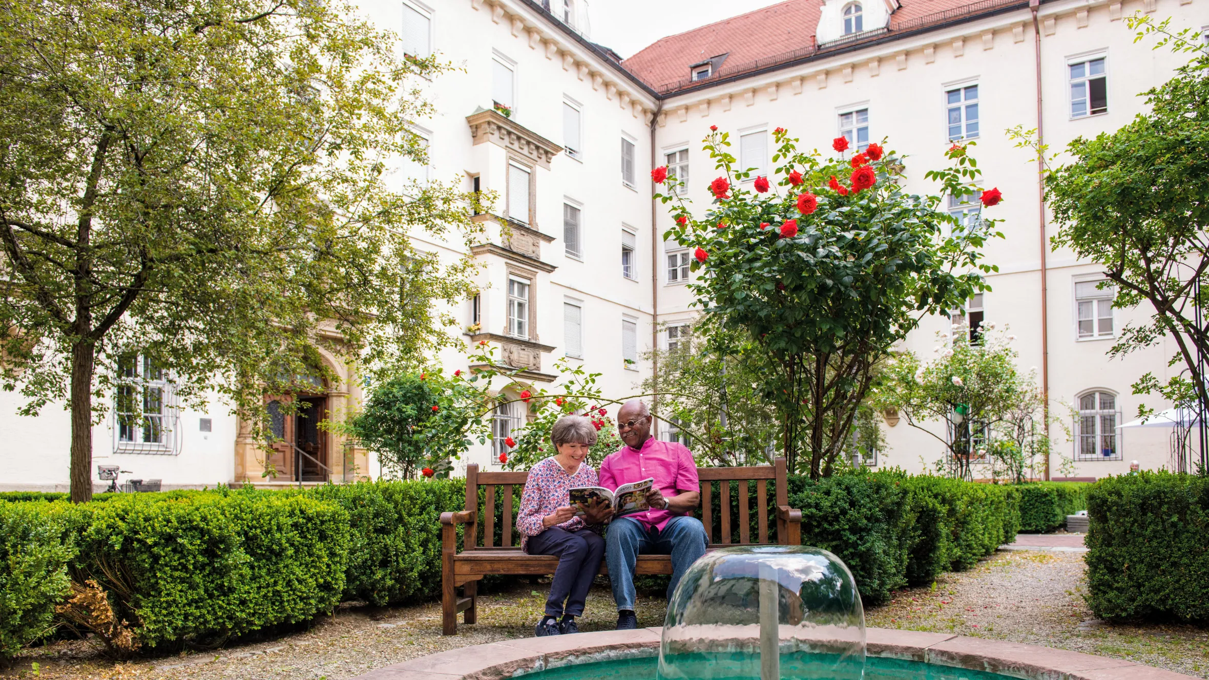 Bewohnerehepaar beim gemeinsamen Zeitschriften lesen in der Außenanlage des Mathildenstifts