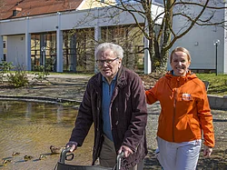 Eine Pflegerin geht mit einem Gast aus der Tagespflege spazieren.