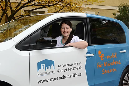 Eine junge Frau sitzt in einem Auto und lächelt aus dem Fenster in die Kamera