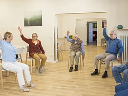 Eine Pflegerin macht mit Gästen der Tagespflege gymnastische Übungen.
