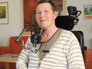 Eine Frau mit kurzen Haaren sitzt in einem großen Elektrorollstuhl.