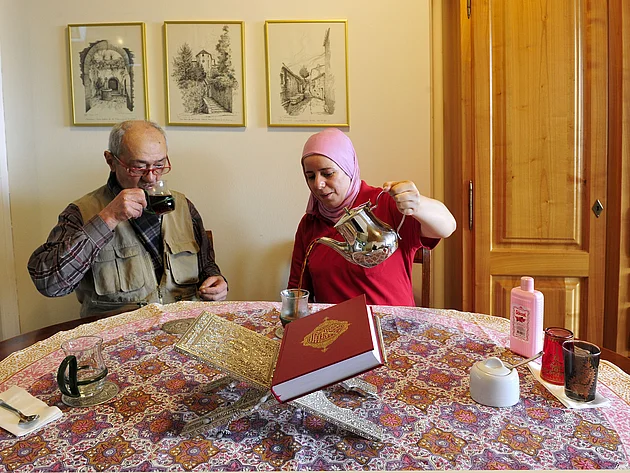 Ein Mann und eine Frau mit Hidschab trinken gemeinsam Tee. Vor ihnen liegt eine Ausgabe des Koran. 