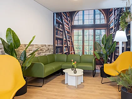 ein schöner Raum mit Bücherregalen im Hintergrund und gemütlichem Sofa und Sessel im Vordergrund.